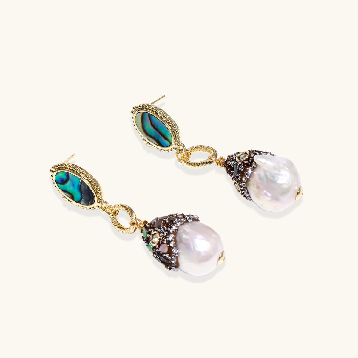Gold drop earrings with iridescent abalone studs, rope links, jeweled caps and white baroque pearls on cream background