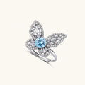 Sterling silver ring with blue moissanite center stone surrounded by clear stones in butterfly wing pattern on white background