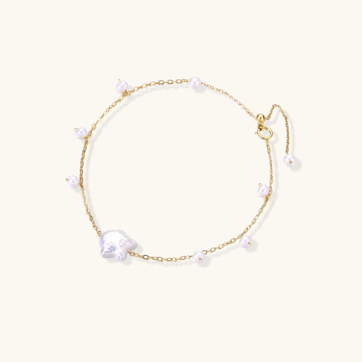Delicate gold chain bracelet with baroque pearl centerpiece and small freshwater pearls on cream background.