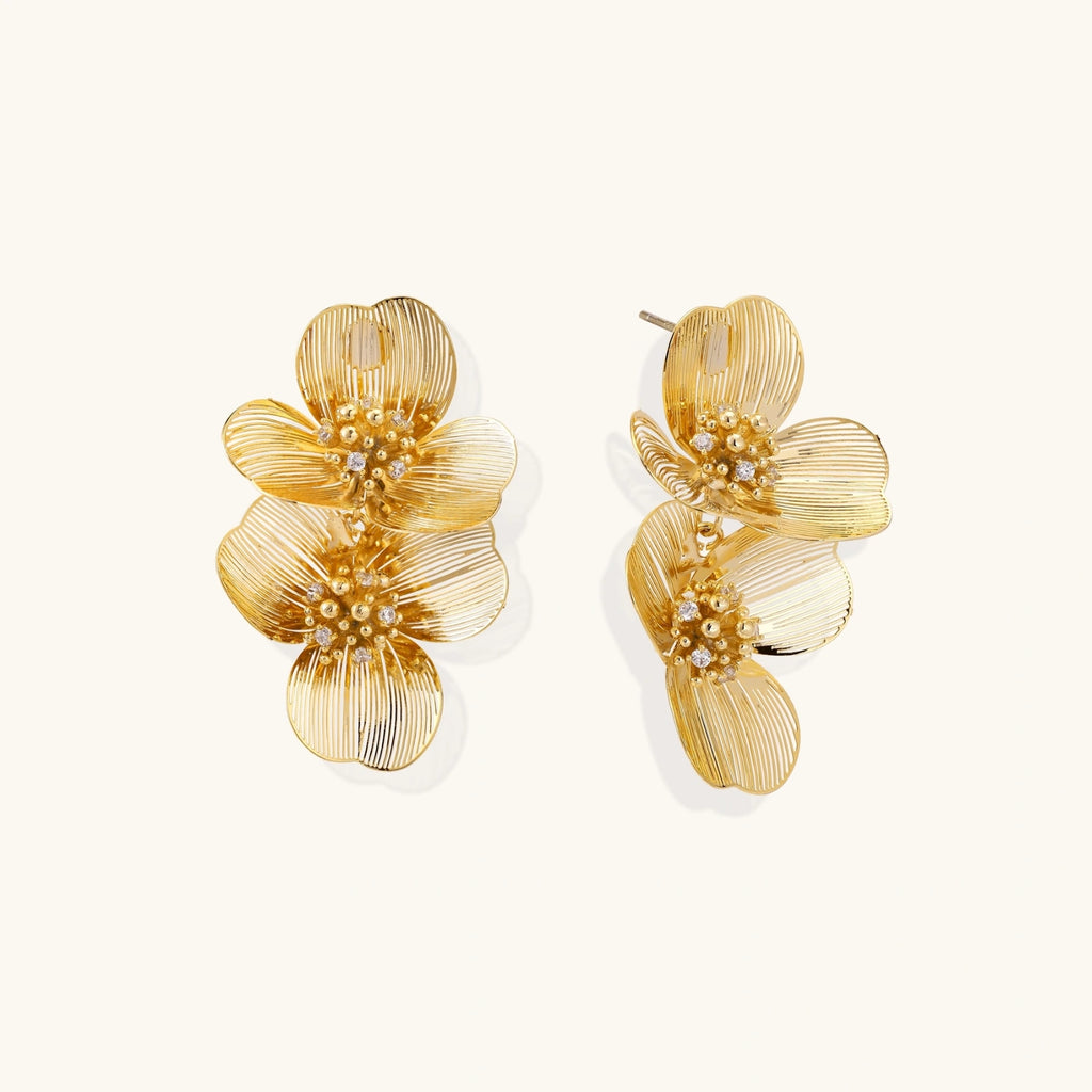 Pair of gold-plated double flower earrings with textured petals and crystal centers on cream background.
