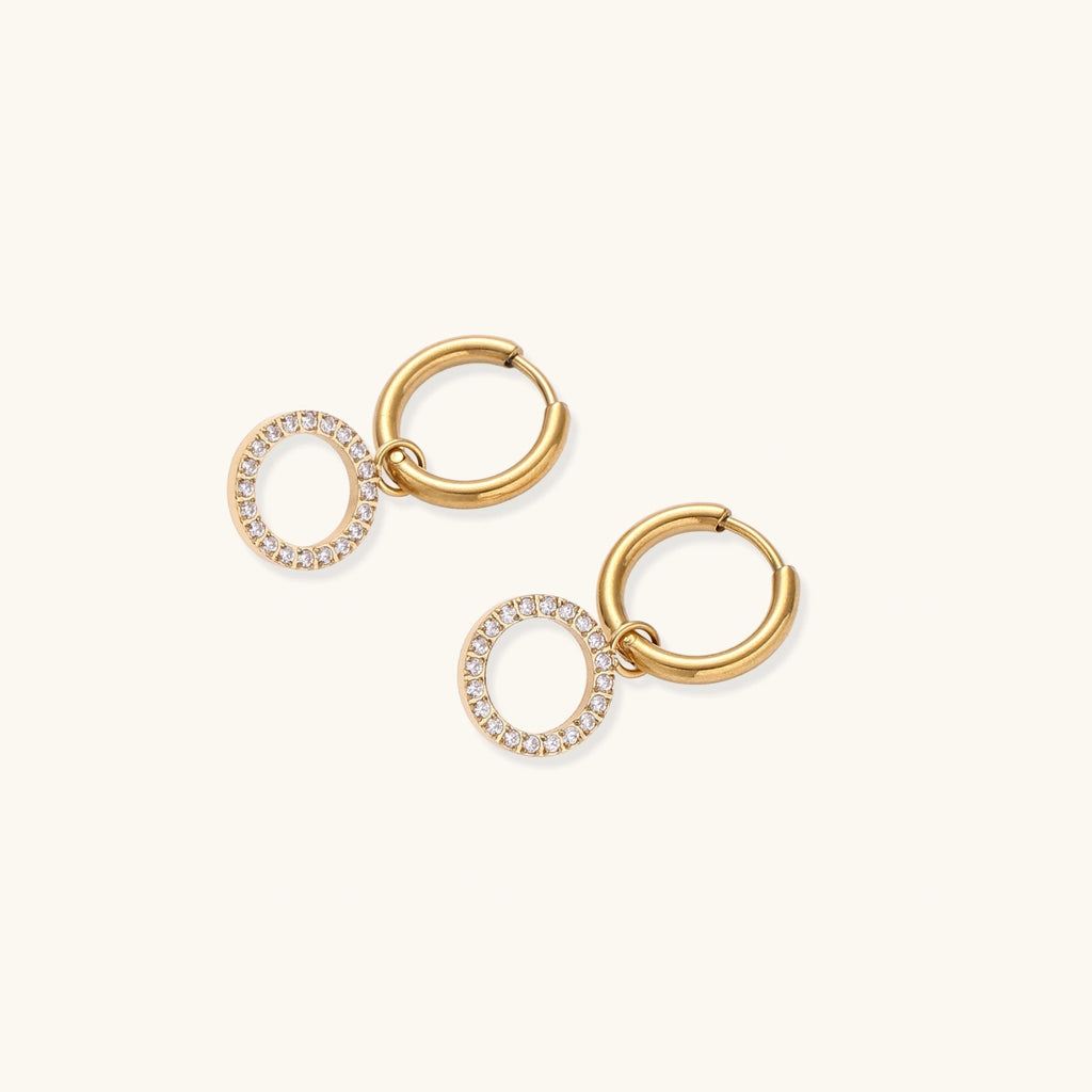 Gold-plated huggie hoop earrings with CZ-studded open circle charms on beige background